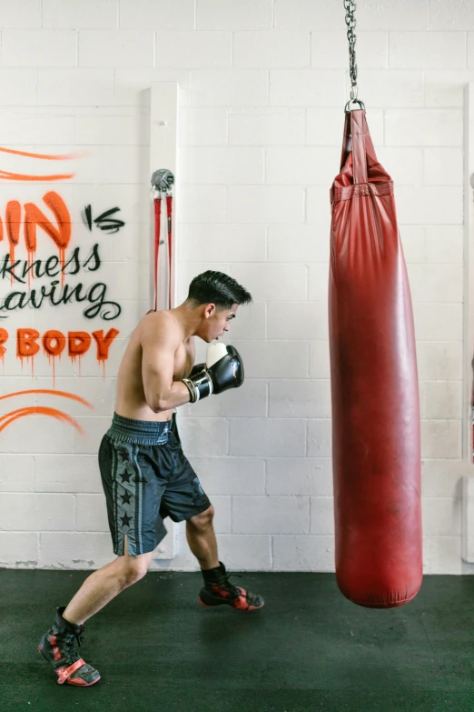 a man standing next to a punching bag, by Robbie Trevino, happening, pacing, darren quach, profile image, orange gi