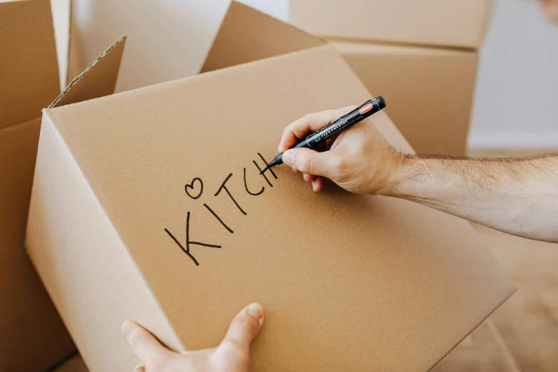 a person writing on a cardboard box with a marker, by Niko Henrichon, pexels contest winner, kitch, moving, a labeled, tan