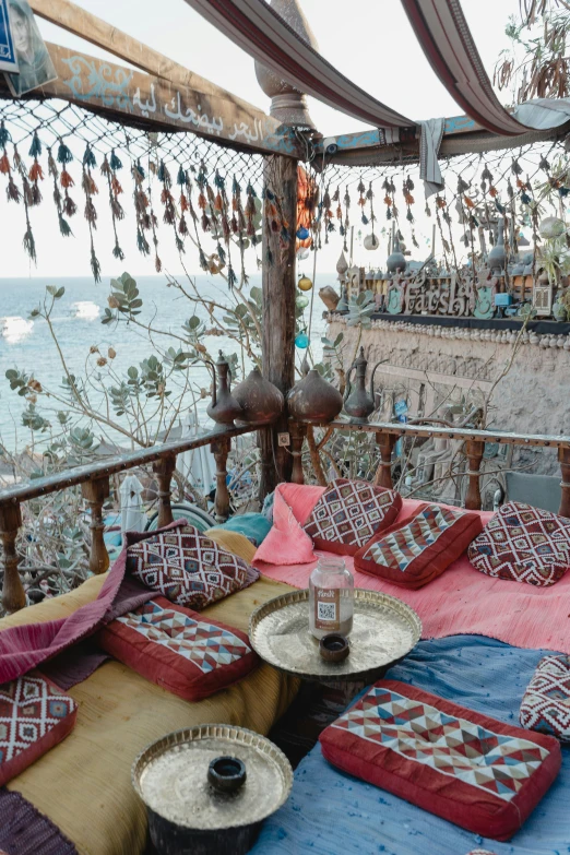 a bed sitting under a canopy next to the ocean, inspired by Riad Beyrouti, trending on unsplash, arabesque, behind bar deck with bear mugs, lebanon kirsten dunst, high view, taken in the early 2020s