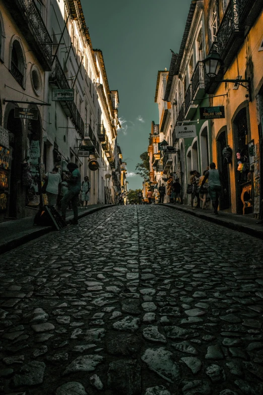 a cobblestone street in a city at night, an album cover, by Alejandro Obregón, pexels contest winner, streets of salvador, sunny day time, background image, buildings covered in black tar