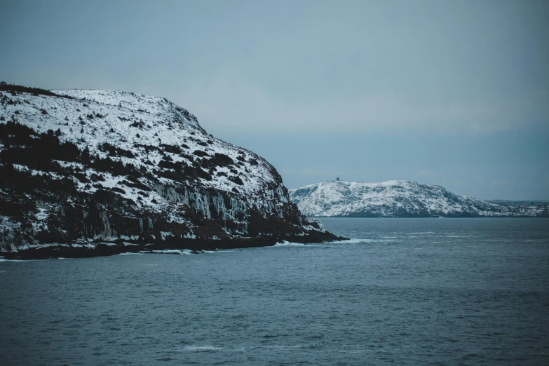 a body of water with a mountain in the background, by Roar Kjernstad, pexels contest winner, hurufiyya, snow flurries, coastal cliffs, two medium sized islands, thumbnail