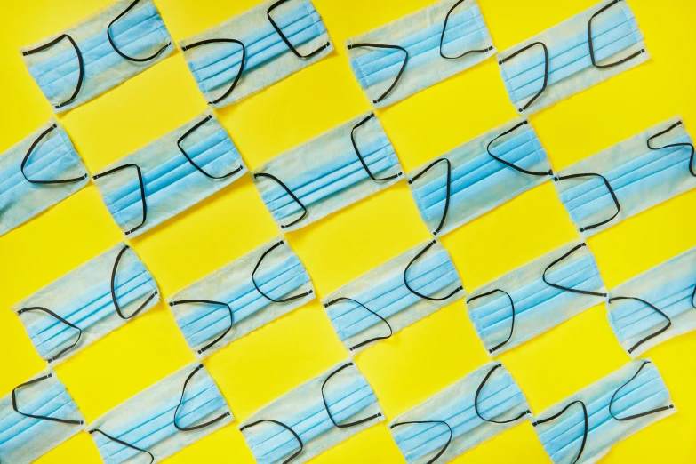 a close up of a piece of paper with glasses on it, an album cover, trending on pexels, op art, yellow and blue ribbons, medical mask, repeating pattern, 6k