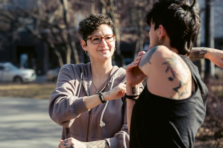 a couple of women standing next to each other, a tattoo, by Harriet Zeitlin, pexels contest winner, sunny day time, queer woman, person in foreground, carefully crafted