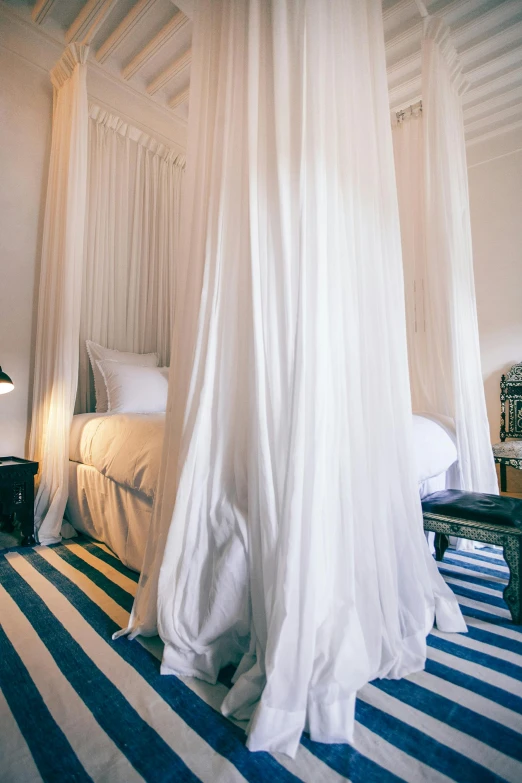 a white canopy bed sitting inside of a bedroom, inspired by Riad Beyrouti, stripes, hotel room, long flowing fabric, high angle