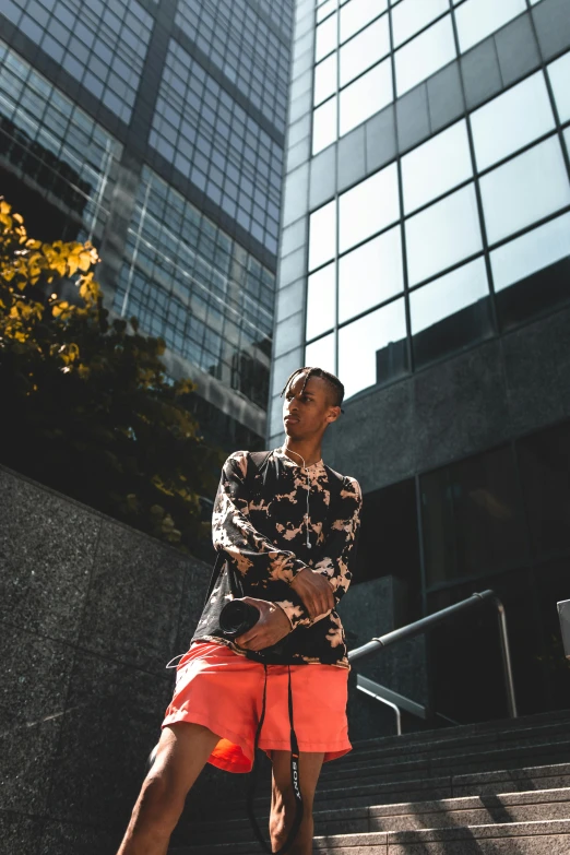 a man standing in front of a tall building, by Cosmo Alexander, pexels contest winner, handsome hip hop young black man, patterned clothing, orange and black tones, very very low quality picture