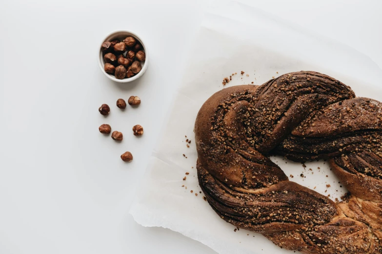 a loaf of bread sitting next to a bowl of nuts, pexels contest winner, hurufiyya, braided brown hair, on a white table, dark chocolate hair colour, circle