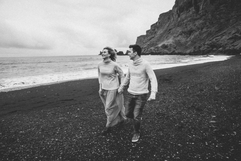 a black and white photo of two people walking on a beach, wearing a sweater, jovana rikalo, happy couple, colorless