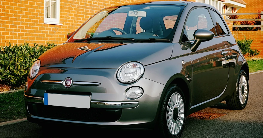 a small car parked in front of a brick building, a picture, profile image, grey, thumbnail, magnificent oval face