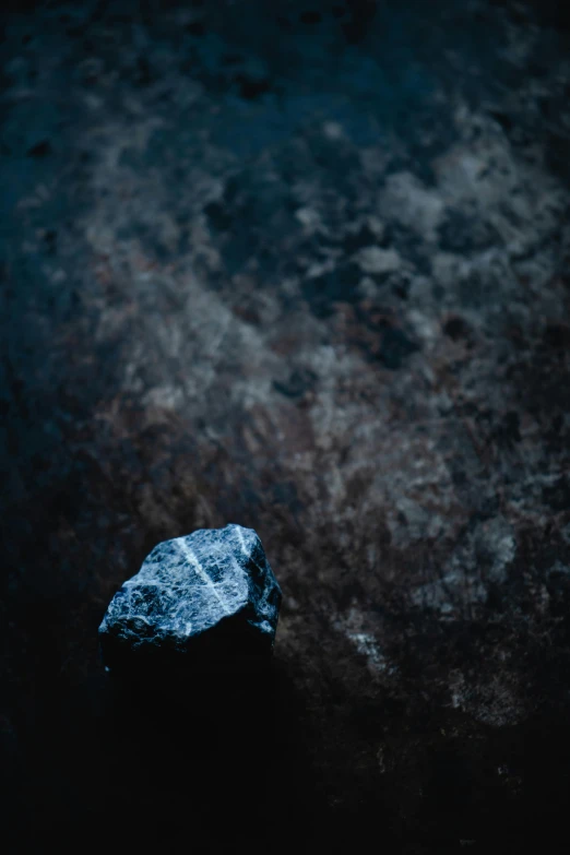 a rock sitting on the ground in the dark, an album cover, by Jacob Toorenvliet, unsplash, blue silver and black, mining scrap metal, chemistry, slate