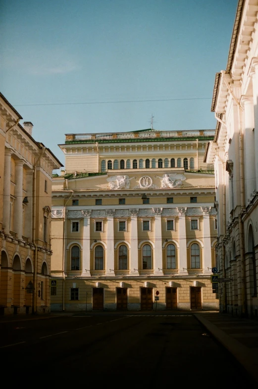 a large building with a clock on top of it, inspired by Illarion Pryanishnikov, neoclassicism, sunfaded, there are archways, view from ground, many buildings
