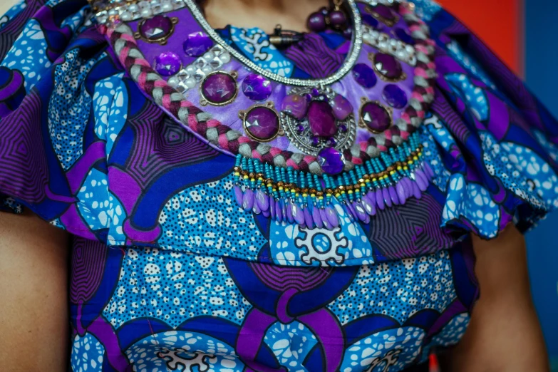 a close up of a woman wearing a colorful dress, by Ingrida Kadaka, afrofuturism, necklace on display, purple and blue colour palette, embedded with gemstones, blue colored traditional wear