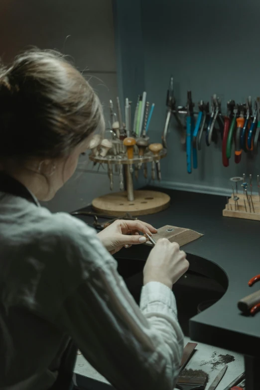 a woman sitting at a desk in front of a computer, an engraving, pexels contest winner, gunsmithing, 2 0 2 1 cinematic 4 k framegrab, hammershøi, jewelry