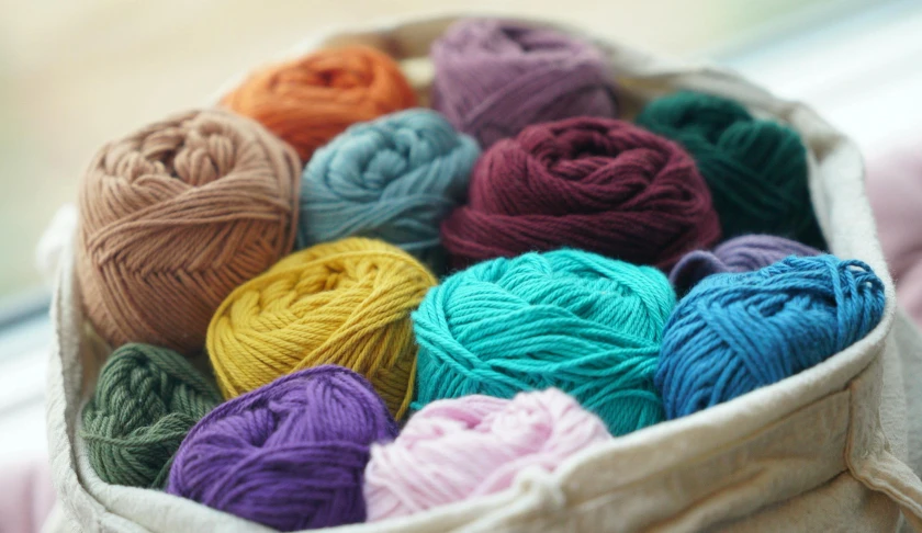 a basket full of balls of yarn sitting on a window sill, a cross stitch, inspired by Toss Woollaston, pexels, pastel deep colours, middle close up, fibres trial on the floor, full product shot