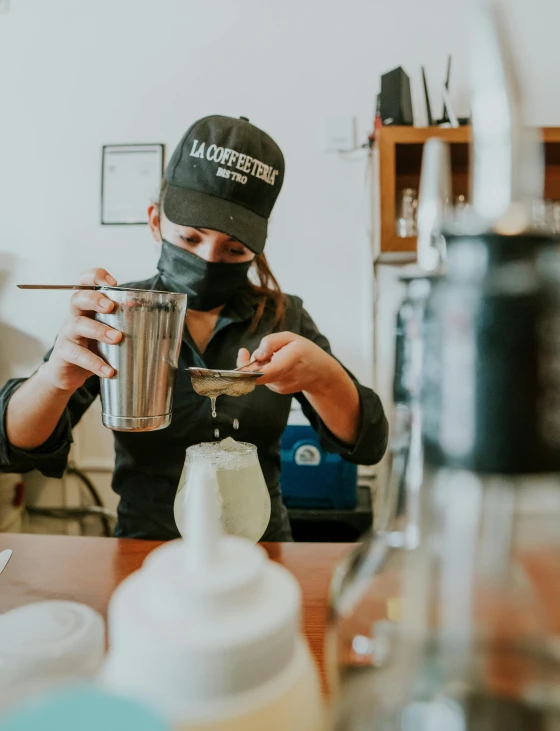 a person sitting at a table with a cup of coffee, inside a glass jar, mixing drinks, wearing facemask and sunglasses, alchemist lab