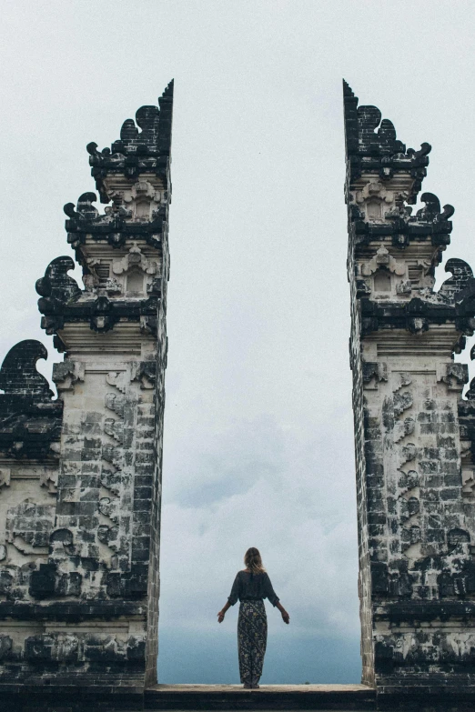 a woman standing in front of a gate, a statue, pexels contest winner, bali, black domes and spires, arched back, looking down