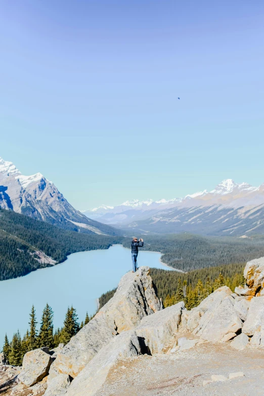 a man standing on top of a mountain next to a lake, banff national park, wide river and lake, award-winning photo, panoramic