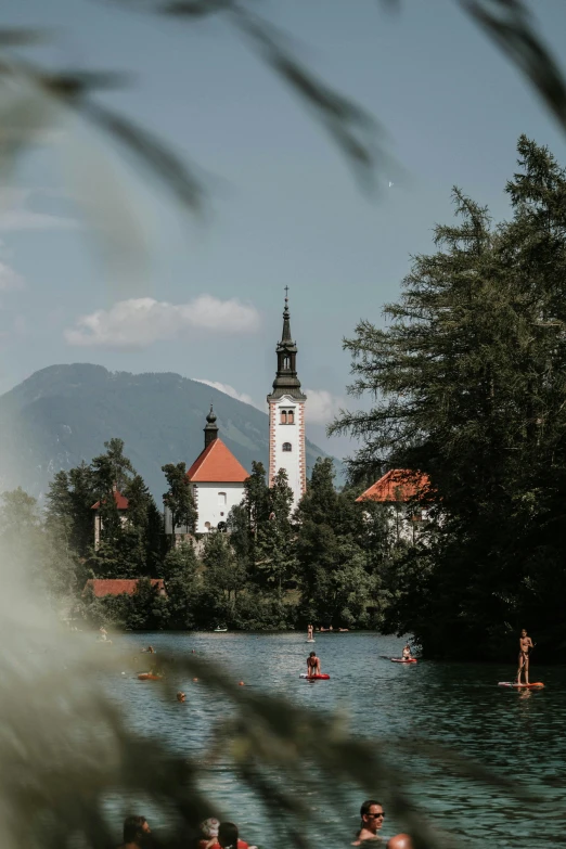 a group of people riding paddle boards on top of a lake, by Sebastian Spreng, pexels contest winner, visual art, black domes and spires, in a park and next to a lake, slovenian, whitewashed buildings