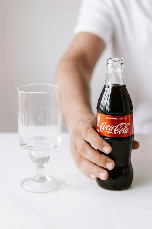 a person sitting at a table with a bottle of coke, glassware, with clear glass, traditional medium, natural tpose