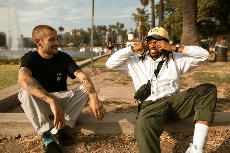 a couple of men sitting next to each other, a portrait, unsplash, visual art, long beach background, dreads, taken in the early 2020s, gang clothing