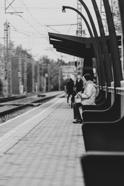 a man sitting on a bench at a train station, a black and white photo, by Tamas Galambos, pexels contest winner, couple, trending on imagestation, sittin, in a suburb
