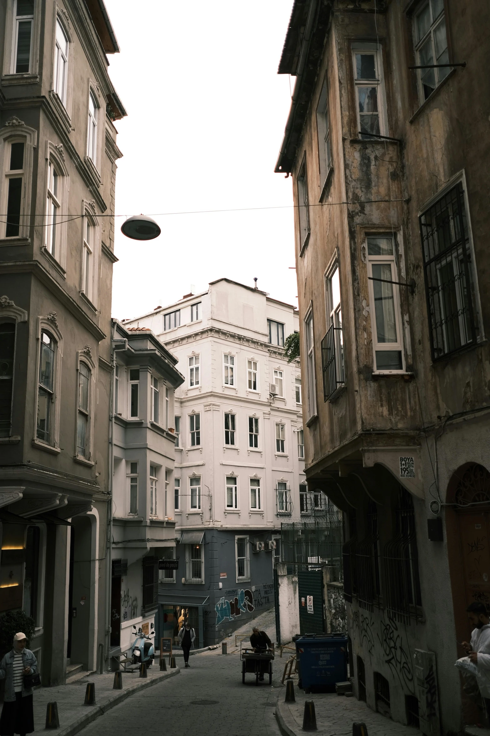 a group of people walking down a street next to tall buildings, a picture, inspired by Niyazi Selimoglu, renaissance, old town, exterior photo, square, muted colors