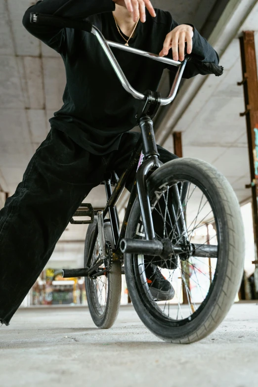 a man riding a bike on top of a cement floor, up close, kick flip, bulky build, black