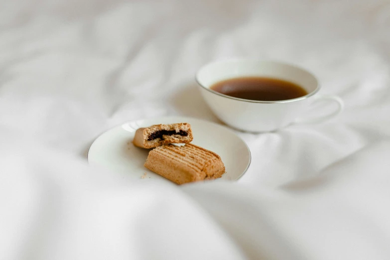 a white plate topped with a pastry next to a cup of coffee, unsplash, sōsaku hanga, licorice allsort filling, lying in bed, on a pale background, a pair of ribbed