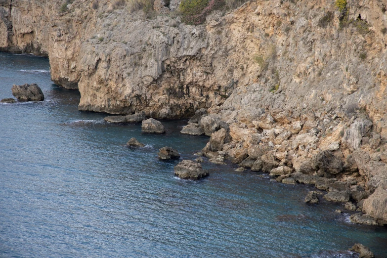 a group of people standing on top of a cliff next to the ocean, crystal clear blue water, with lots of dark grey rocks, costa blanca, julia sarda