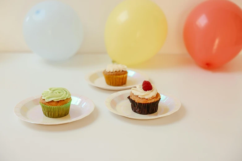 a table topped with plates of cupcakes and balloons, inspired by Wilhelm Hammershøi, unsplash, plain background, white holographic plastic, 3 - piece, multi - coloured