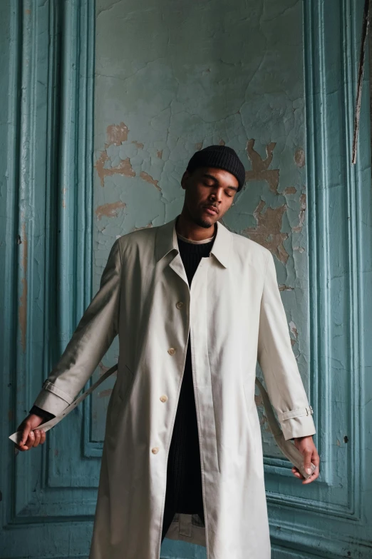 a man in a white coat standing in a room, an album cover, inspired by Christopher Williams, unsplash, he is wearing a trenchcoat, leaning on door, raffael, very tall