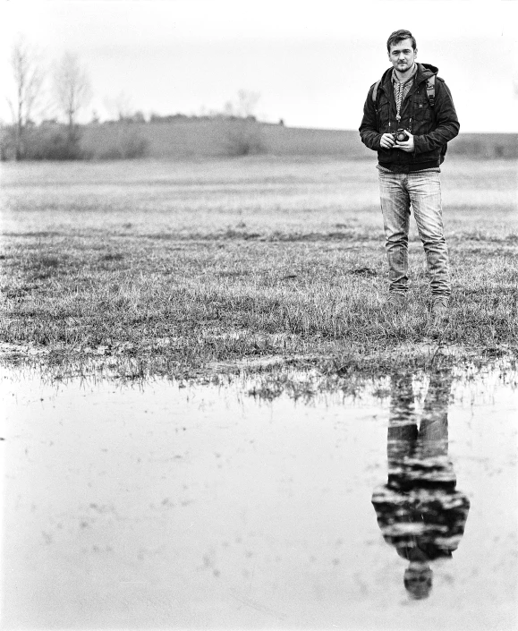 a man standing in a field next to a puddle of water, a black and white photo, art photography, hasselblad photo, selfie, medium format, lowres