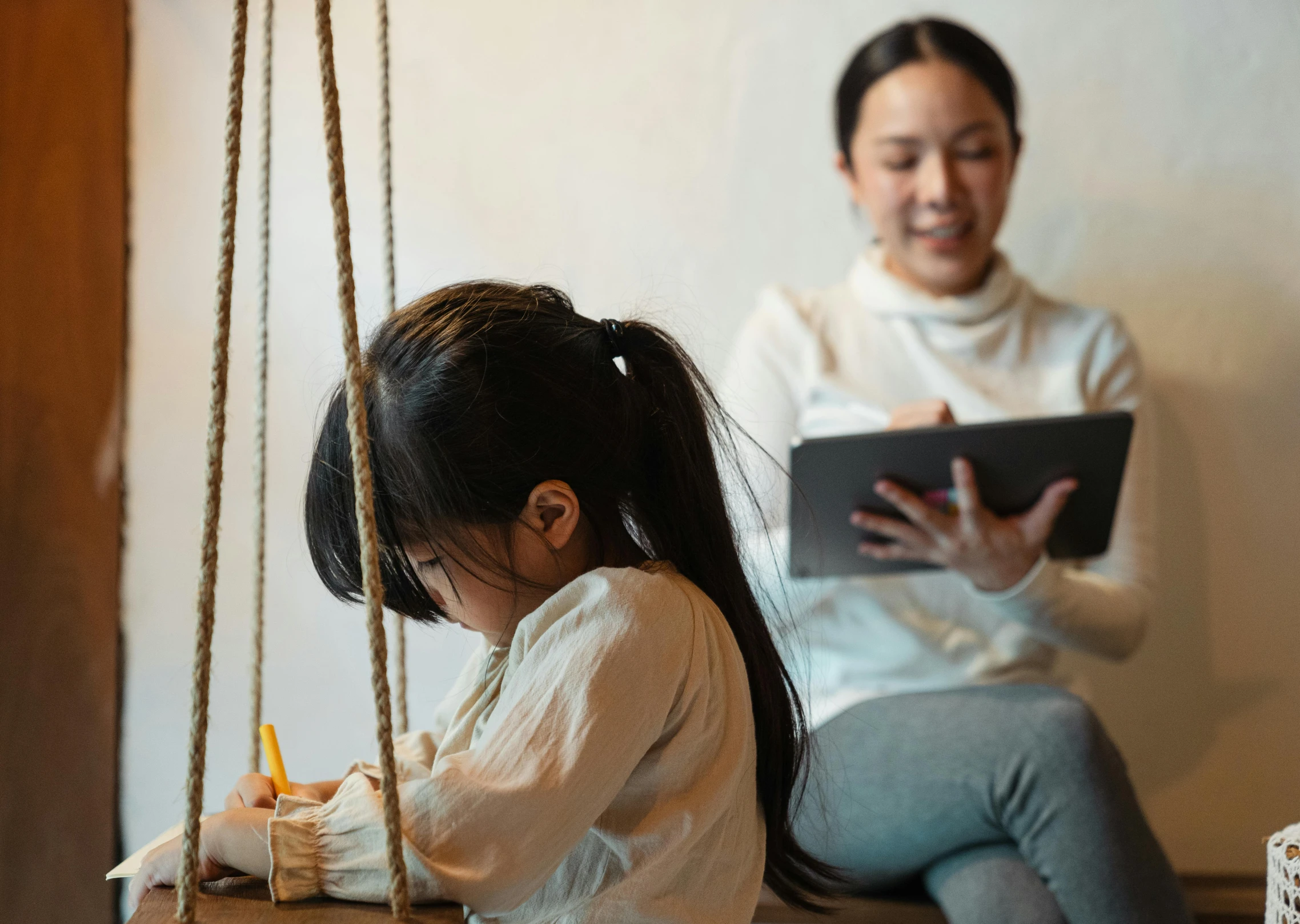 a woman sitting next to a little girl on a swing, a child's drawing, pexels contest winner, writing on a clipboard, asian female, suspenseful, a wooden