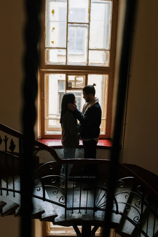 a man and a woman standing in front of a window, pexels contest winner, lviv, low quality photo, indoor scene, holding each other