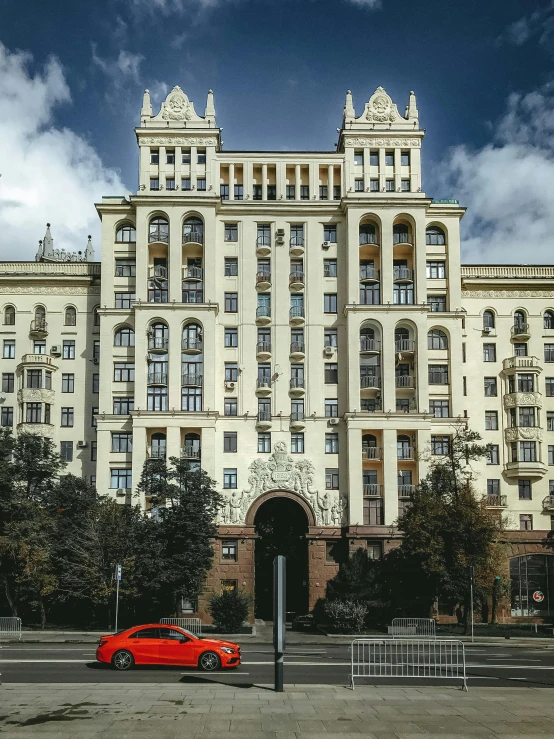 a red car is parked in front of a large building, inspired by Vassily Maximov, pexels contest winner, socialist realism, neo kyiv, yellow windows and details, with stalinist style highrise, 000 — википедия