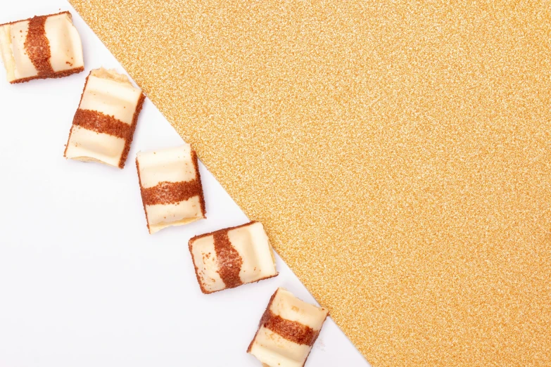 a couple of pieces of food sitting on top of a table, an album cover, inspired by Jacopo Bellini, trending on unsplash, glitter, brown and cream color scheme, cubic blocks mix stripes cuts, full view blank background