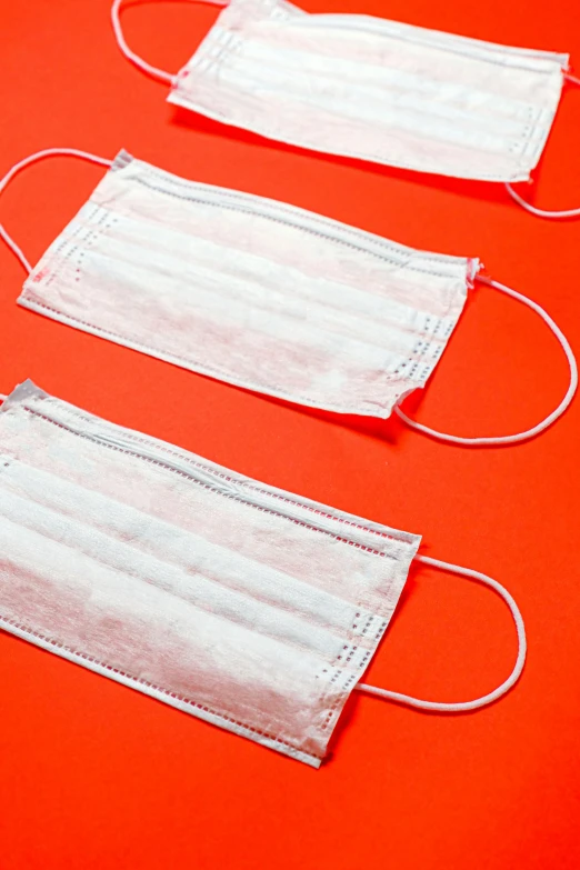 three medical masks on a red background, by Rachel Reckitt, happening, white and orange, surgical supplies, thumbnail, up-close