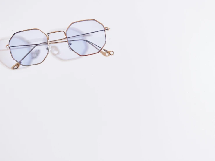 a pair of glasses on a white surface, by Eizan Kikukawa, trending on unsplash, visual art, gold and blue, hexagonal shaped, full view blank background, detailed product shot