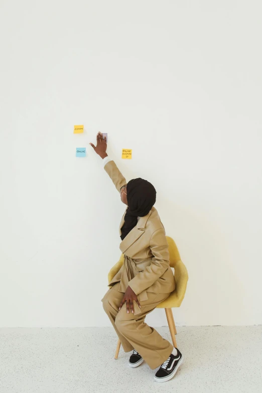 a person sitting on a chair in front of a white wall, on a yellow paper, pointing, aida muluneh, switch