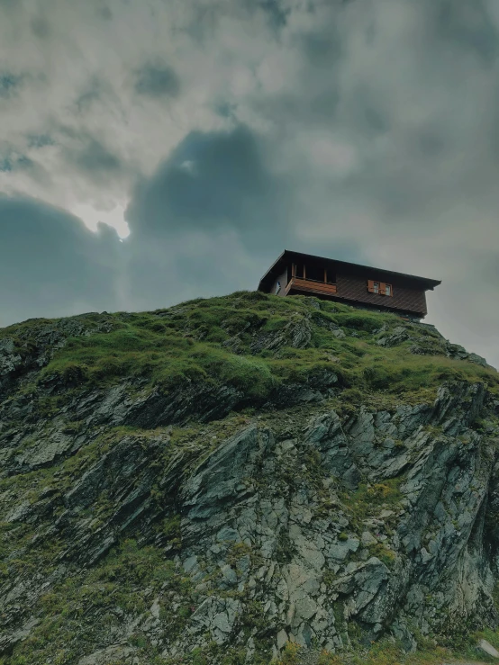 a small house sitting on top of a mountain, inspired by Peter Zumthor, pexels contest winner, renaissance, profile image, moody cinematic atmosphere, brown, low quality photo