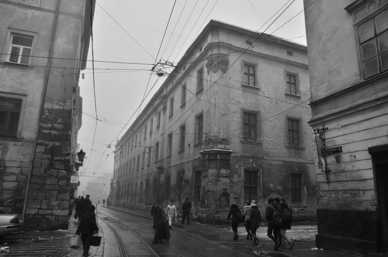 a black and white photo of people walking down a street, danube school, foggy rainy day, old building, covered with wires, lviv