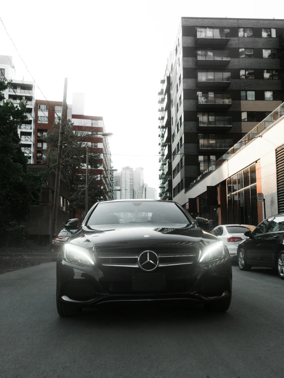 a black car driving down a street next to tall buildings, by Niko Henrichon, pexels contest winner, mercedez benz, front light, on a sidewalk of vancouver, clean detail 4k