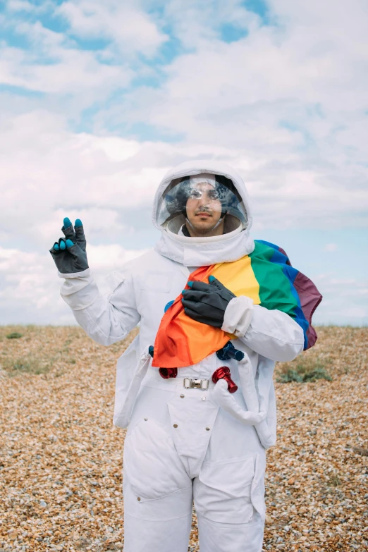 a man in an astronaut suit standing on a beach, pride month, paul davey, cosmic style, waving