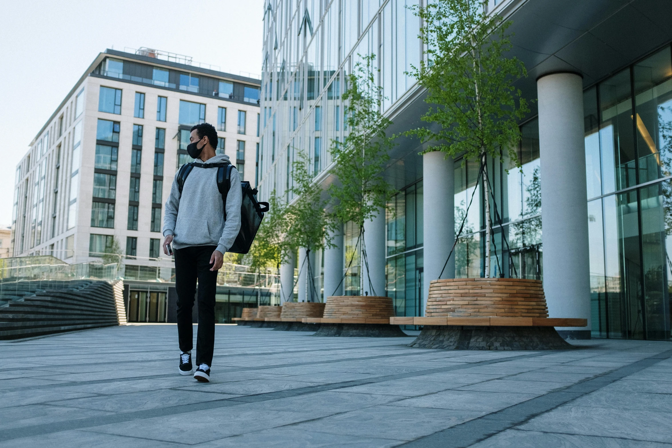 a man walking down a sidewalk in front of a building, a picture, student, sustainable materials, in a cybercity, thumbnail