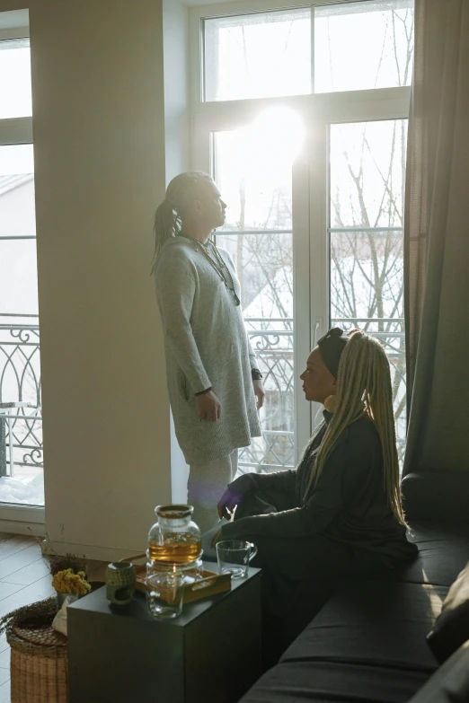 a couple of people sitting on a couch in a living room, inspired by Elsa Bleda, pexels contest winner, renaissance, tea ceremony scene, cold sunshine through window, blonde women, facing each other