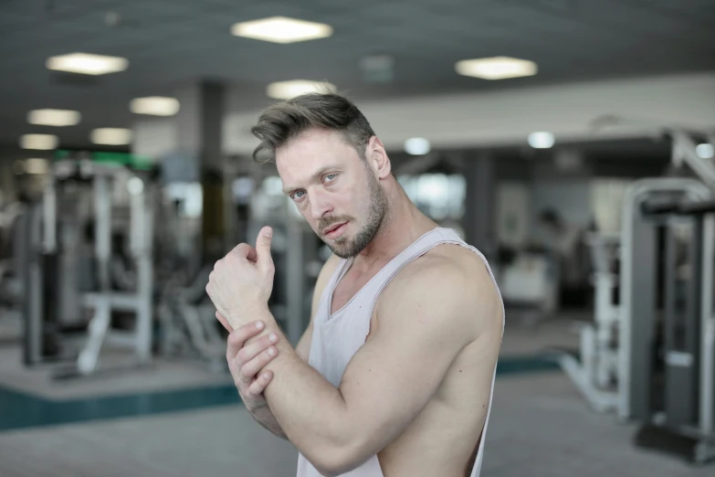 a man in a white tank top standing in a gym, by Adam Marczyński, pexels contest winner, hyperrealism, hand on his cheek, bandage on arms, square, of the muscular