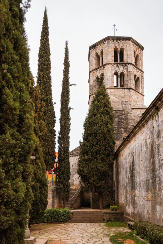 a narrow cobblestone street with a clock tower in the background, romanesque, cypress trees, high view, limestone, towering high up over your view