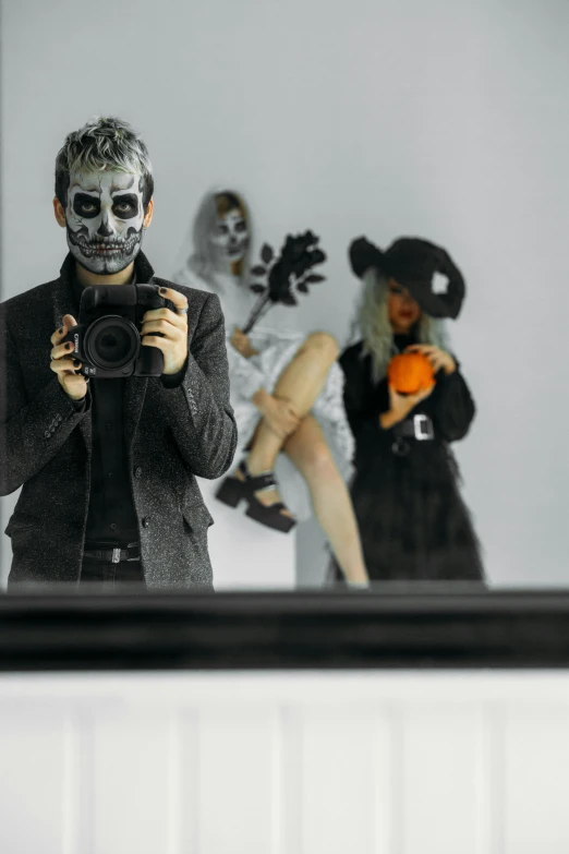 a man standing in front of a mirror holding a camera, inspired by Jodorowsky, pexels contest winner, photorealism, ska skeleton and girlfriend, diverse costumes, black mask, taking a picture