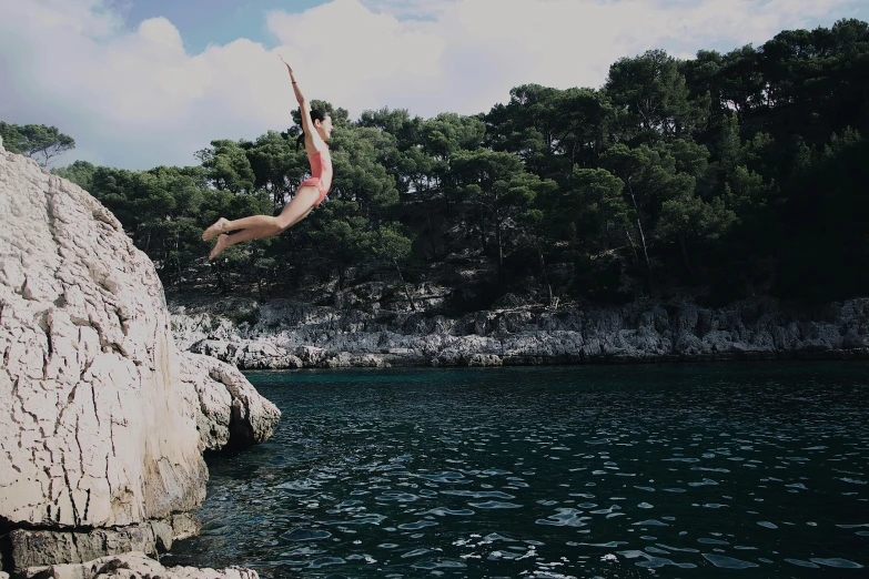 a person jumping off a cliff into a body of water, over a calanque, gofl course and swimming, monia merlo, unsplash 4k