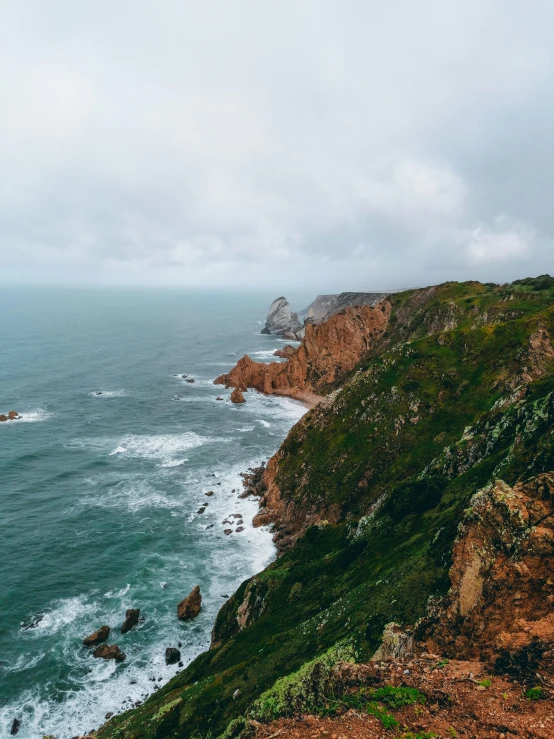 a man standing on top of a cliff next to the ocean, by Jacob Pynas, pexels contest winner, portugal, rainy, panorama view, devils horns