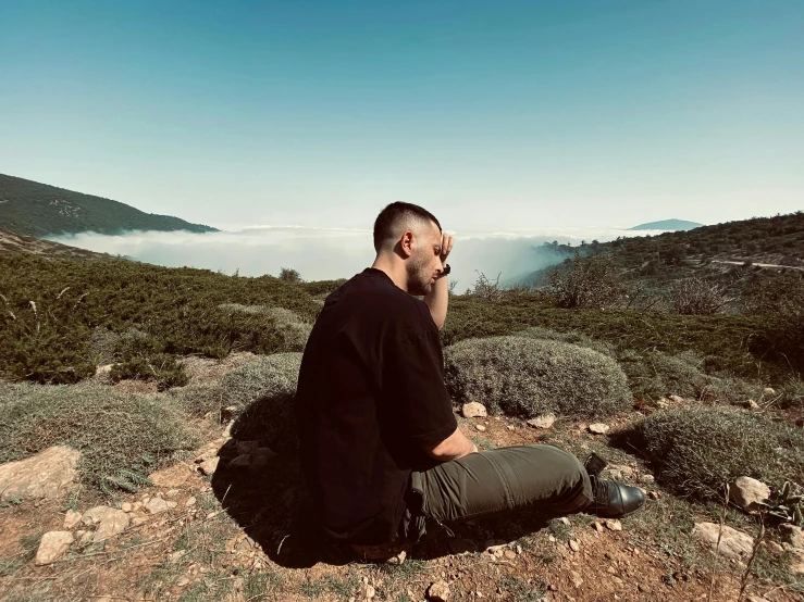 a man sitting on top of a mountain talking on a cell phone, a picture, pexels contest winner, les nabis, mac miller, profile image, thoughtful pose, looking at the ground